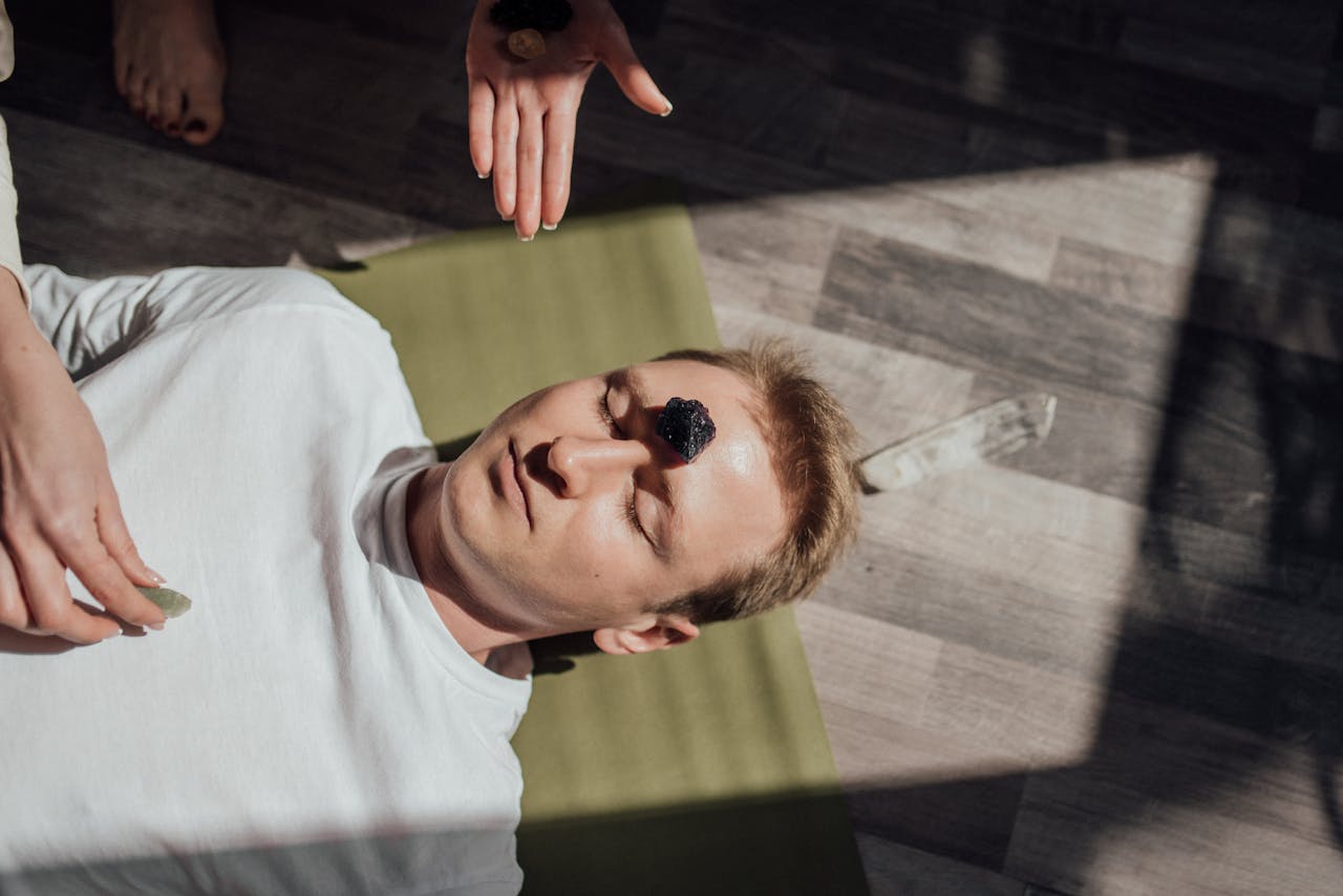 home-img Man lying down with healing crystals for a relaxation therapy session indoors.
